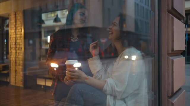 Cute lesbian couple drinking coffee and chatting behind glass window