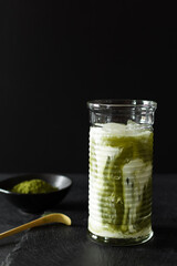 Green matcha iced latte in a long glass on black background.