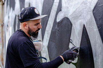 Graffiti artist in action, painting on the wall with aerosol spray paint in a can, wearing...