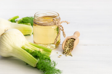 Glass bottle of fennel essential oil with fennel seeds and bulb on wooden table. Herbs alternative medicine background concept