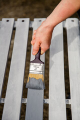 Process of hand painting white timber boards with grey paint using painting brush. 