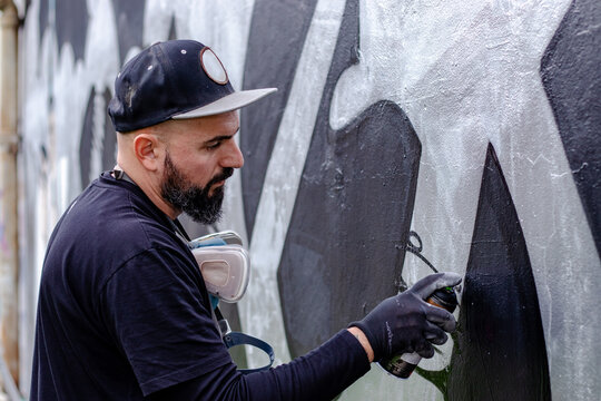 Graffiti artist in action, painting on the wall with aerosol spray paint in a can, wearing protective gloves. Street art culture concept.