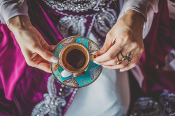 Young girl wearing in beautiful oriental dress holding a cup of traditional Turkish coffee
