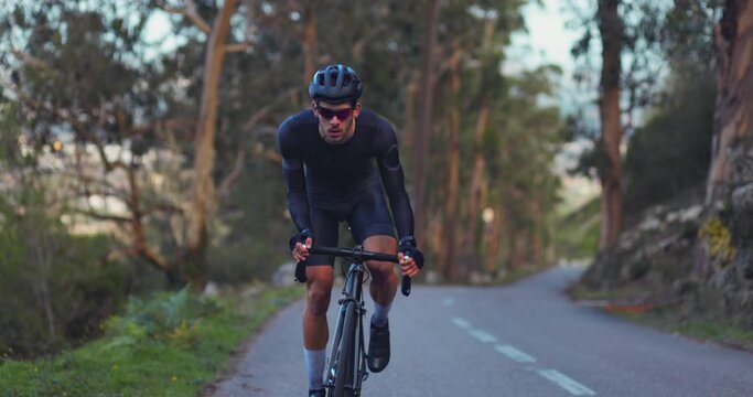 Professional cyclist riding sports bicycle uphill on a forest