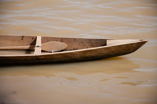 Front half of a wooden fishing boat and paddle on the brown water of the reservoir in Ougadougou, Burkina Faso