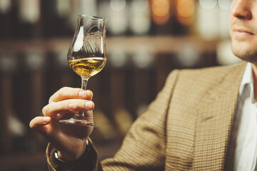 Sommelier holding a glass of whiskey, evaluates the color, smell and taste of alcoholic beverage.