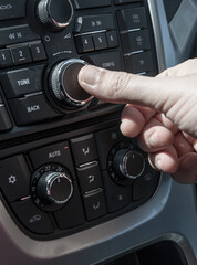 Mano de hombre acciona los controles del equipo de música de un coche moderno con climatizador automático y control de la temperatura