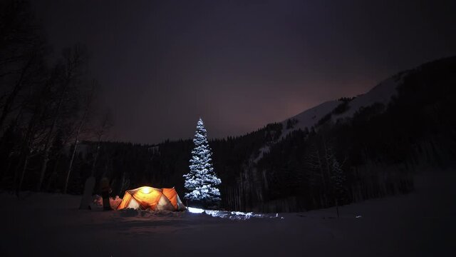 A night sky timelapse of winter camping with a tent in the snow under the stars. 