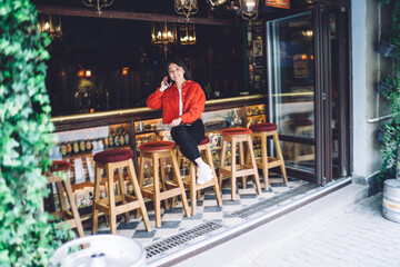 Smiling young ethnic woman having phone conversation in street bar
