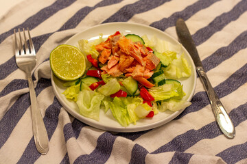 Salmon salad with fresh vegetables on a white plate and a knife and a fork.