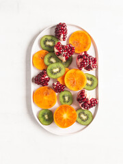 Seasonal fruit - persimmon, kiwi, pomegranate slices on white plate