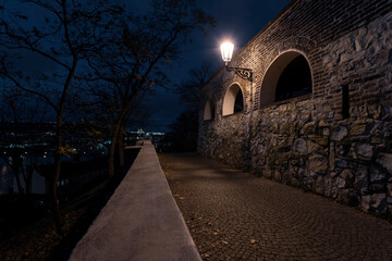 Fototapeta premium light from street lighting and old stone fortress walls from the 15th century and paving blocks on the ground for pedestrians at night in the center of prague in the czech republic and in the backgro