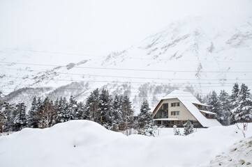 house in the winter forest on the background of snowy mountains