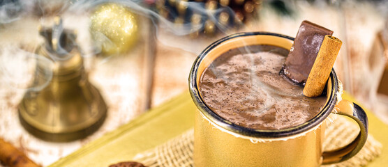 hot chocolate in golden copper mug, hot Christmas or winter drink with cinnamon, smoke or steam.