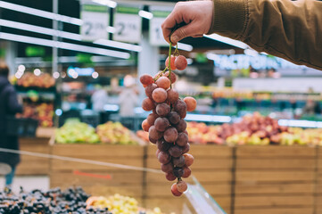 A man in a supermarket holds a bunch of fresh grapes in his hands.