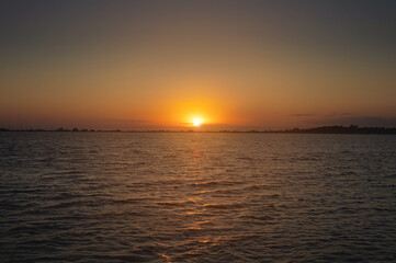 A colorful sunset over a bay or lake with a calm water surface. Late evening. Low key