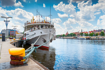 Large boat docked or moored on Customs Quay, view on promenade and boulevards on Odra River embarkment with old town in background in Szczecin, Poland - obrazy, fototapety, plakaty