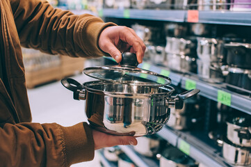 A man in a supermarket holds a metal pot with a lid.