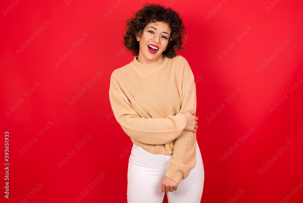 Sticker Young beautiful Arab woman wearing beige sweater against red background laughing.