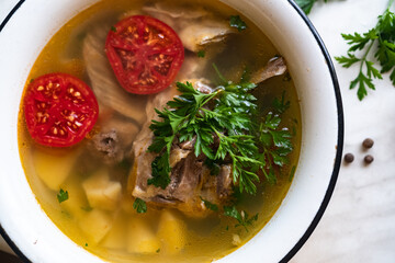 fish soup with carp, potatoes, parsley, tomato in enamel bowl stands on a board
