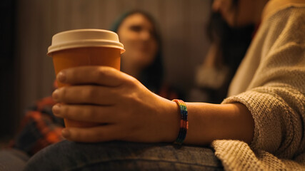 Close view: Cup of coffee in hand of lesbian woman chatting with girlfriend in cafe
