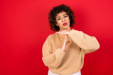 Young beautiful Arab woman wearing beige sweater against red background feels tired and bored,...