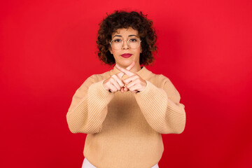 Young beautiful Arab woman wearing beige sweater against red background has rejection angry...