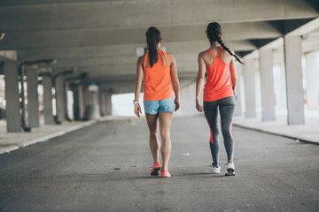 Two female friends jogging on the city street under the city road overpass.They relaxing after...