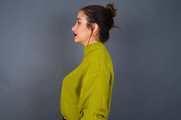 Young beautiful hispanic woman wearing green sweater against gray background looking to side, relax...