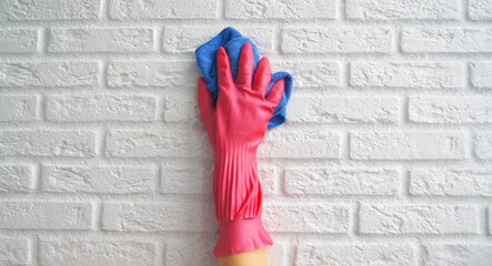 Hand in pink rubber glove washes the white brick wall cleaner