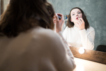 Beautiful brown-haired woman in white sweater looks in the makeup mirror
