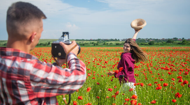 man and woman having romantic date in poppy flower field with photo camera, photographing