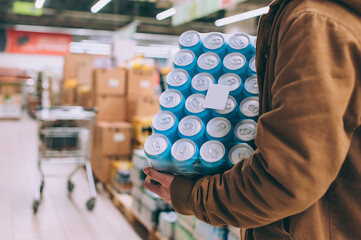 A shopper in a supermarket holds a package of beer in his hands.