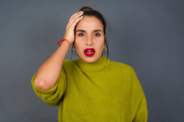 Embarrassed Young beautiful hispanic woman wearing green sweater against gray background with...