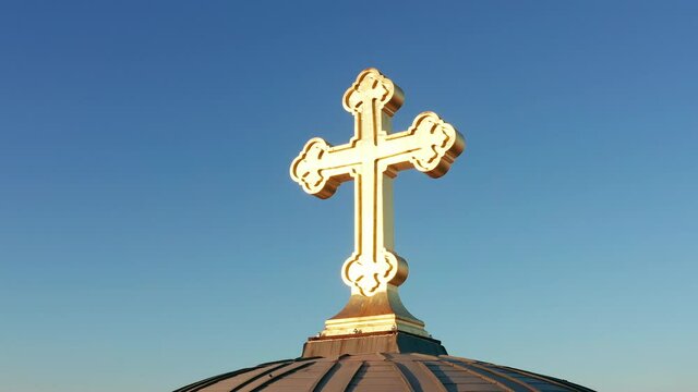 Shiny golden cross against clear blue sky. Crucifix on top of the dome of an orthodox christian cathedral illuminated by sunlight. Symbol of the faith in god made of gold.