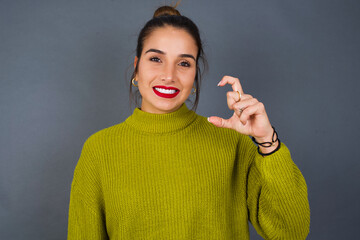 Fototapeta premium Young beautiful hispanic woman wearing green sweater against gray background pointing up with fingers number nine in Chinese sign language Jiu