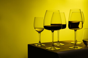 Different glass goblets with white and red wine stand against the yellow light.Glasses of different shapes and heights.Air bubbles are visible in the glasses. Sommelier.Space for text. Assorted wines.