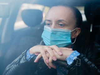 Portrait of a sad woman in a protective mask sitting at the wheel of a car. Concept - depression, female problems