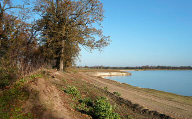 A lake created by a sand excavation. Some deciduous trees and shrubs. Beautiful sunny morning with clear blue skies in the fall.

