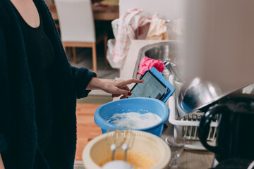 Woman standing in kitchen and cooking while using digital tablet for recipe