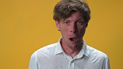 Young man making funny silly facial emotions isolated on yellow background. Weird dorky face of a handsome young man in white shirt. High quality 4k resolution footage. 