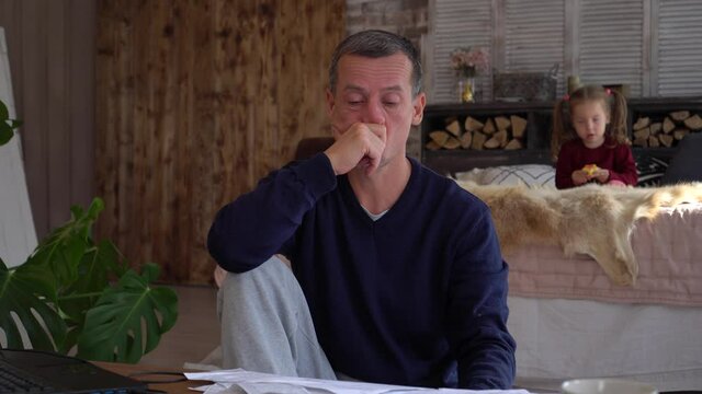 Stressed dad works from home with kid. Remote working with a family during COVID-19 Lockdown. Financial crisis. Little daughter distracts jumps and plays noisily 