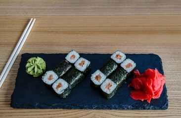 rolls on a black plank with ginger and wasabi on the table