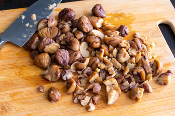 Obraz na płótnie Canvas Chopped Chestnuts on a Cutting Board: Chopping roasted chestnuts on a bamboo cutting board to make chestnut dressing or stuffing