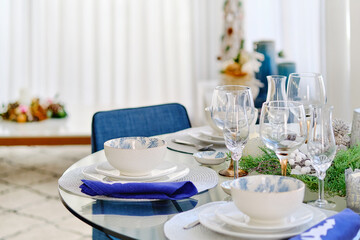 Christmas dinner and New Year event celebration concept. Close up view white dishware blue napkins decoration on the table ready for quest reception, ornate table setting with candle and xmas wreath