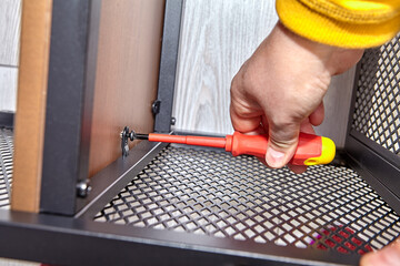 Assembler is mounting metal flat pack furniture using screwdriver.