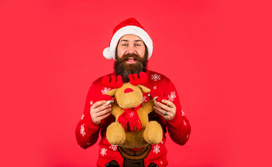 Plush deer. Hipster man hold Christmas gift. Happy man playful mood. Happy new year. Helping Santa Claus. Symbol of Christmas. Christmas eve. Gifts for kids. Dear Santa. Bearded man reindeer toy