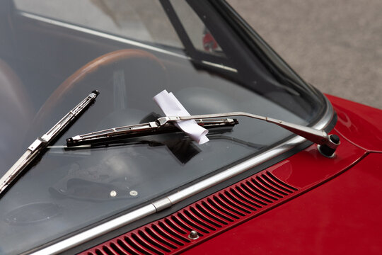 Closeup of a parking violation ticket behind a windshield wiper on a classic car