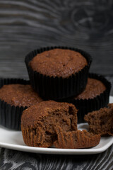 Oatmeal chocolate muffins. Drawn up on a silver platter. One is broken to show a cut. On black pine boards.