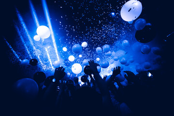 Rave party. Silhouettes of concert crowd in front of bright stage lights and confetti. 